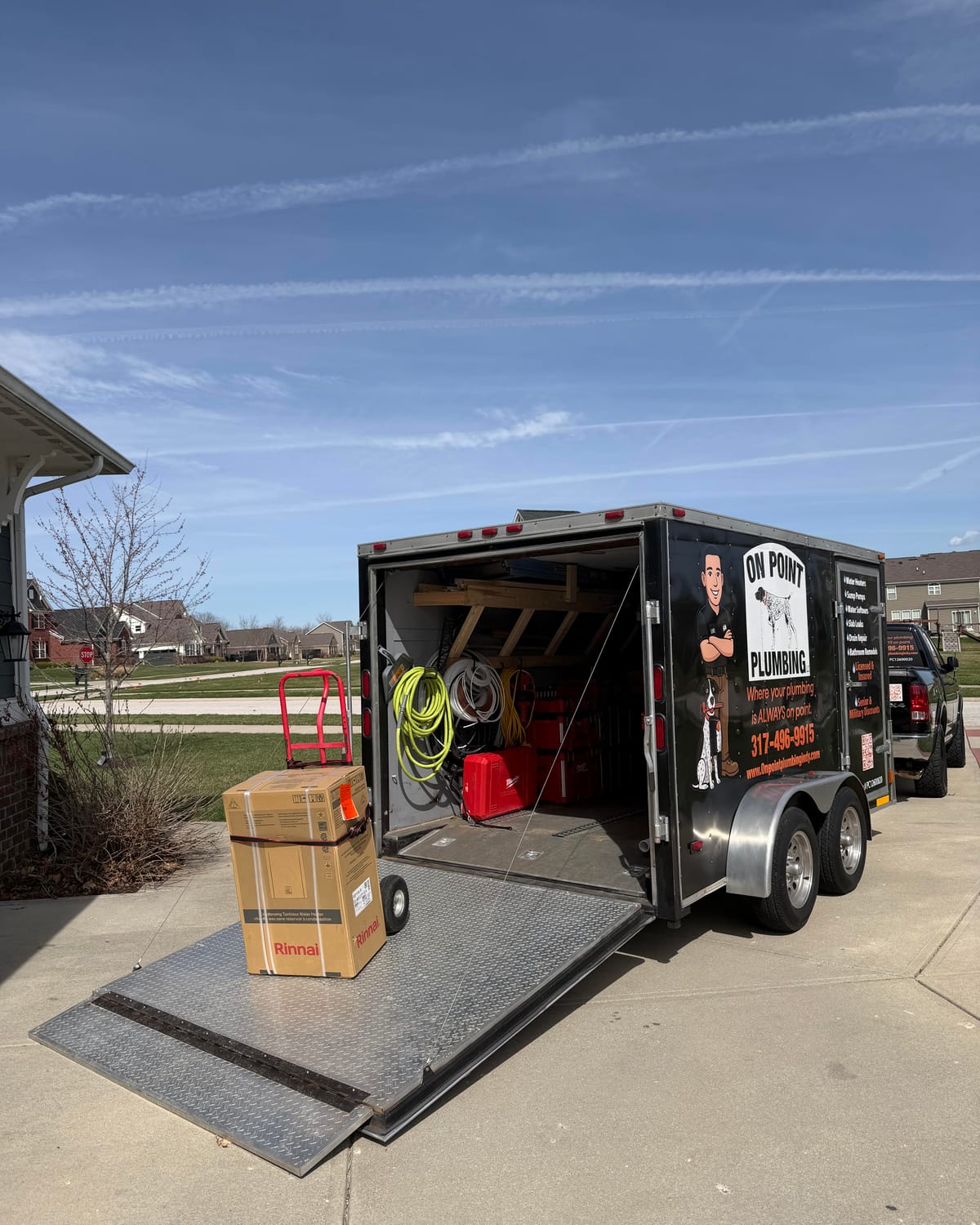 On Point Plumbing's trailer open in a driveway with a new Rinnai water heater ready to install