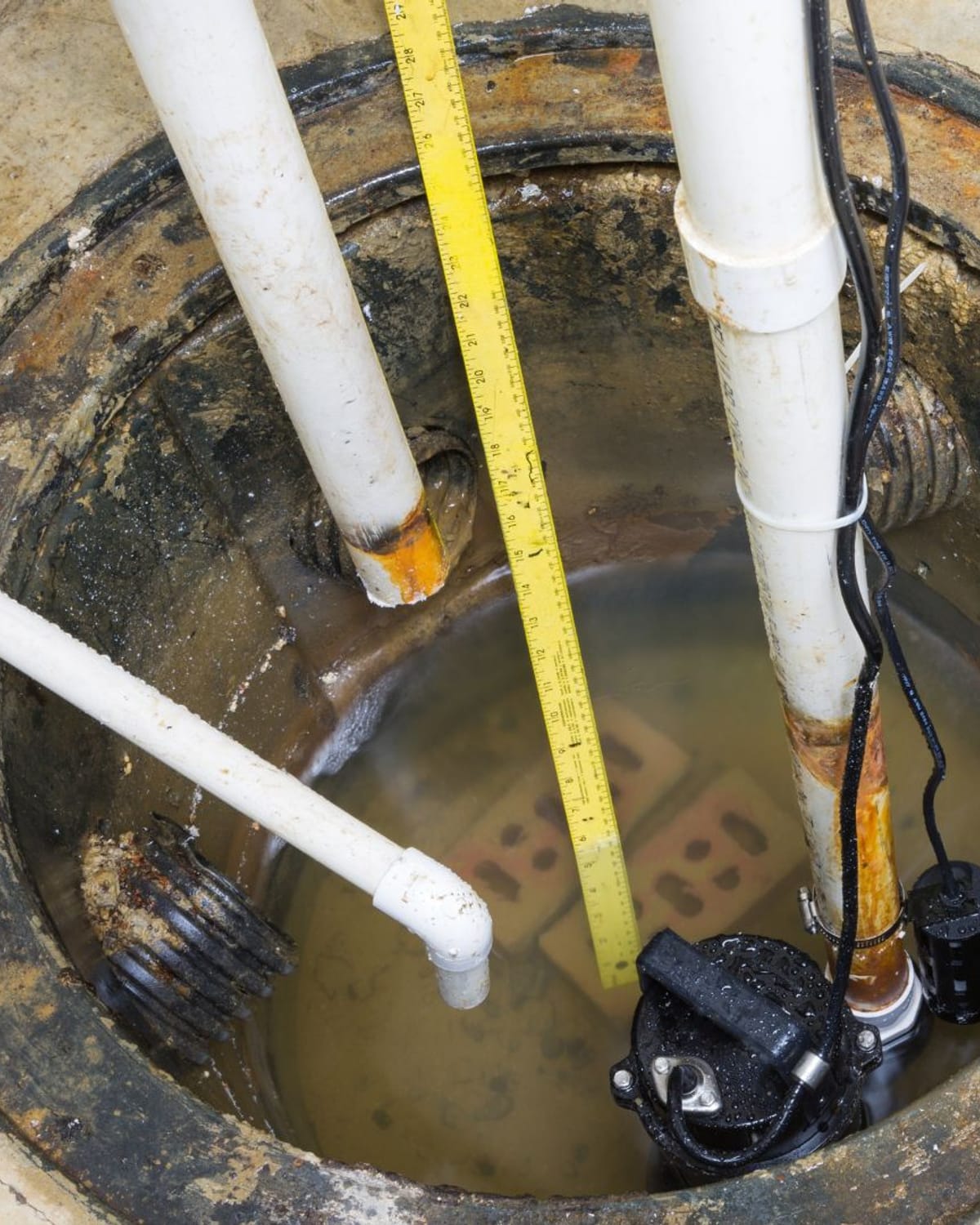 Sump pit and discharge plumbing being measured during a repair