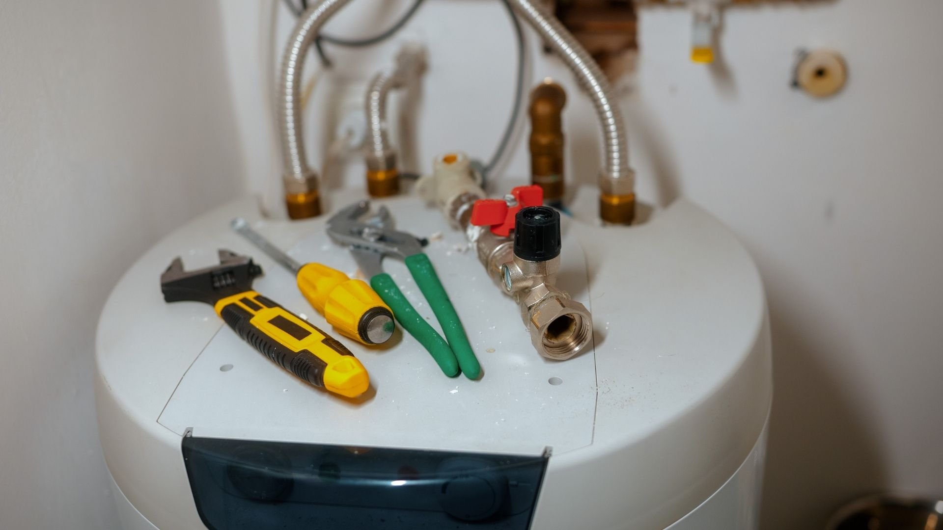 Plumbing tools and valves on white water heater with flexible pipes
