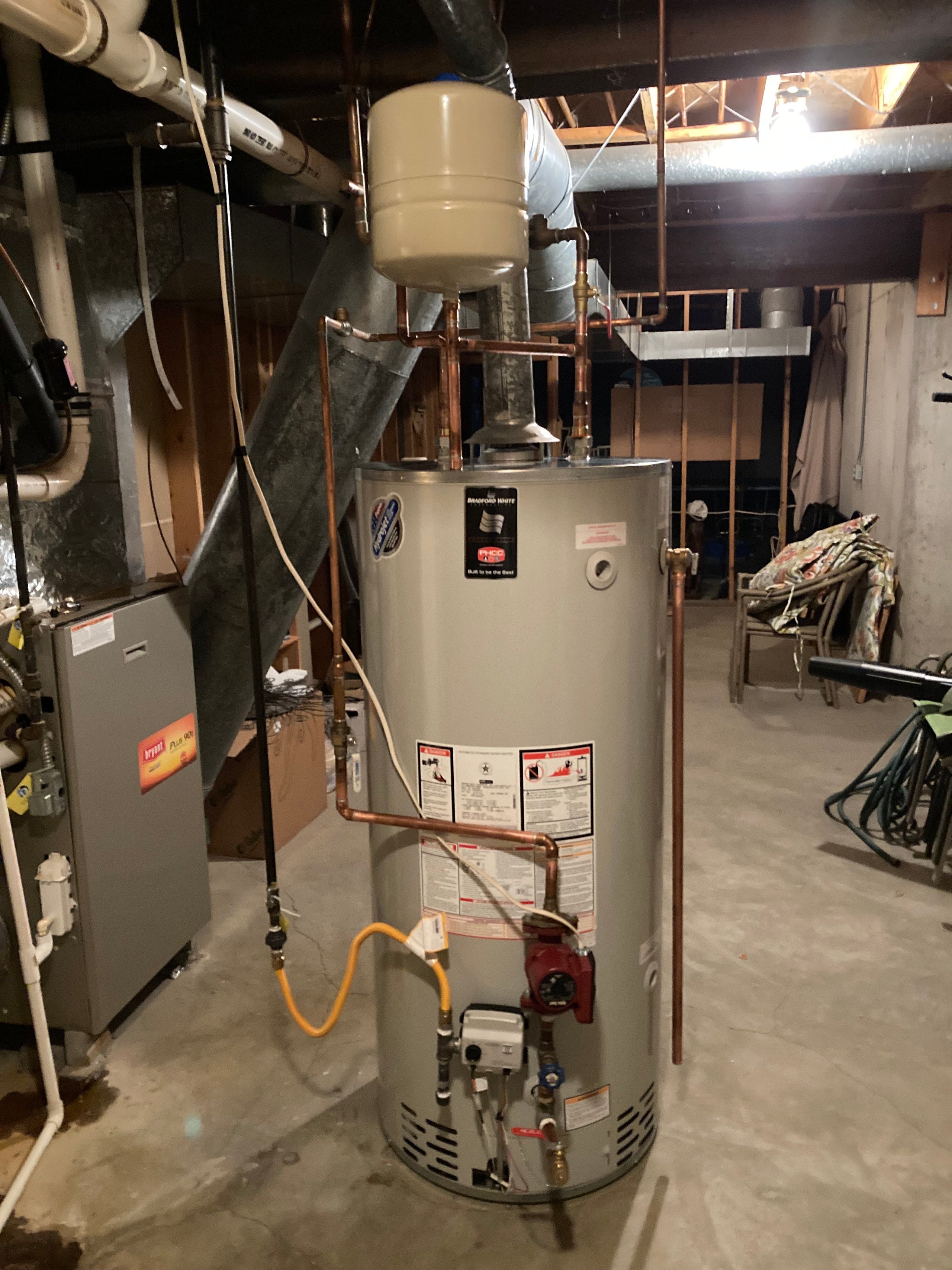Large water heater with copper plumbing pipes in basement utility room
