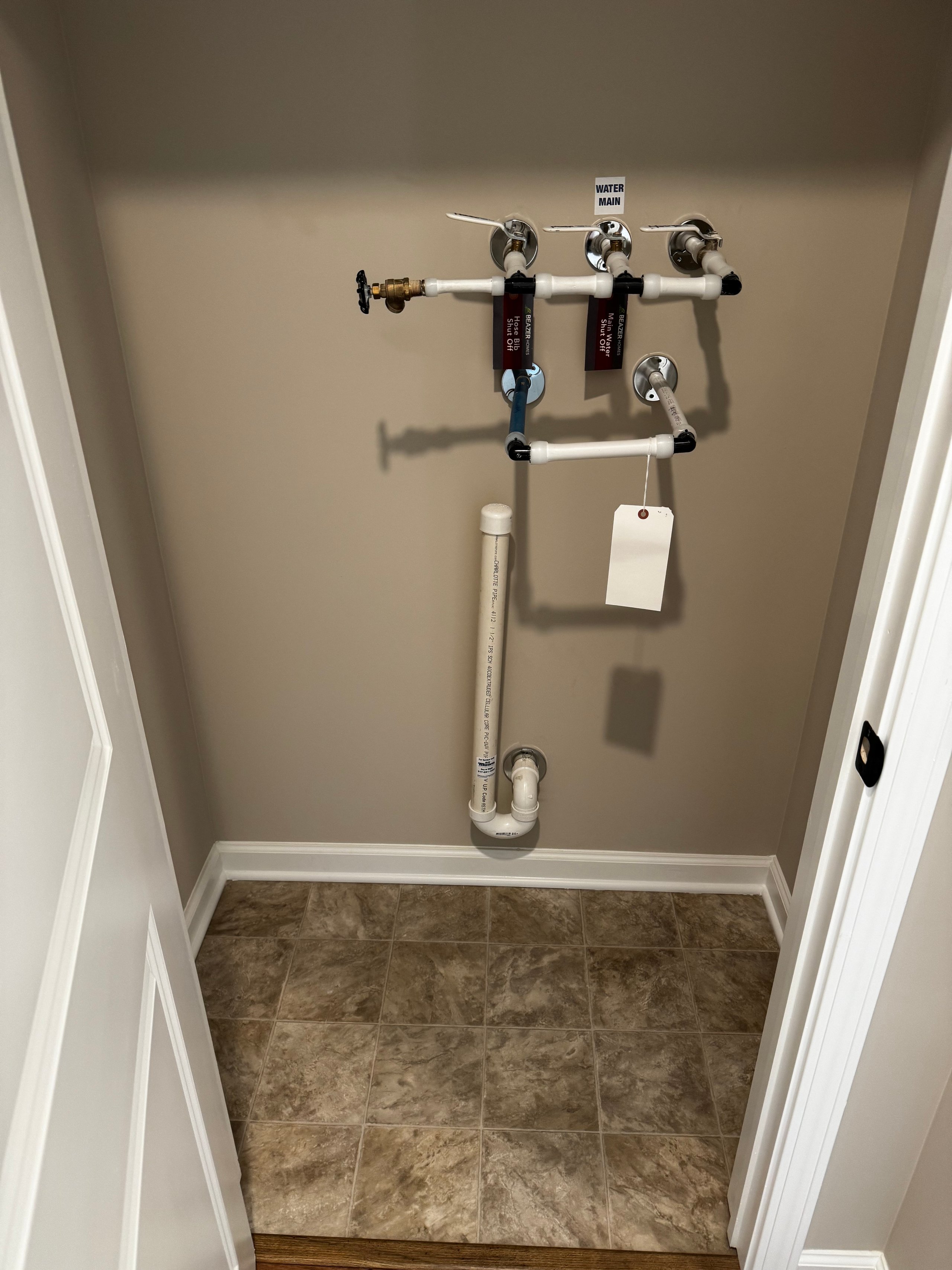 Water main plumbing valves in a small utility closet with tiled floor