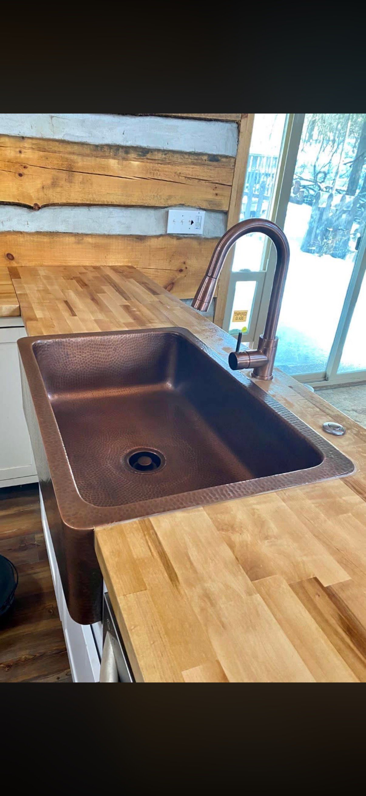 Copper kitchen sink with bronze faucet on wooden butcher block countertop
